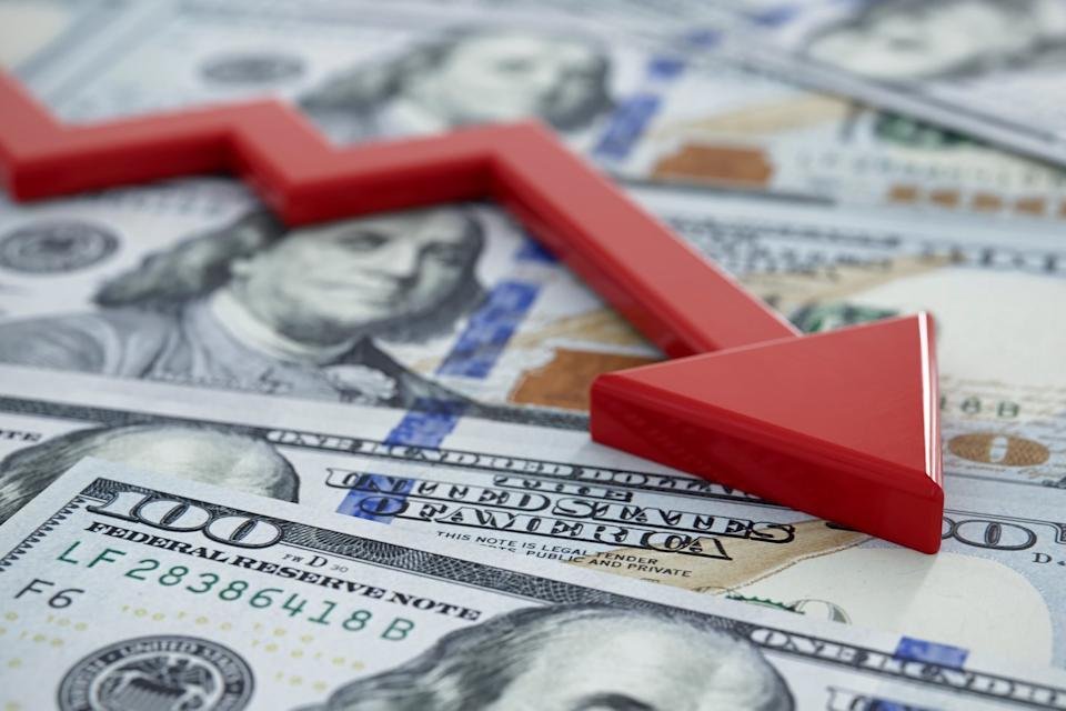 A chart line going down over hundred-dollar bills.