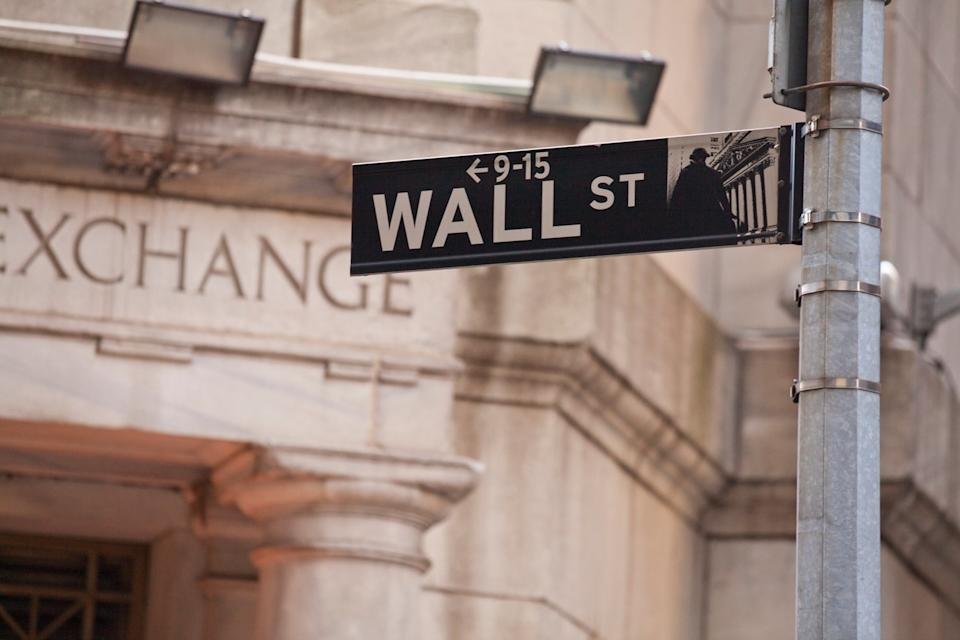 A photo of the Wall Street street sign with the stock exchange in the background.
