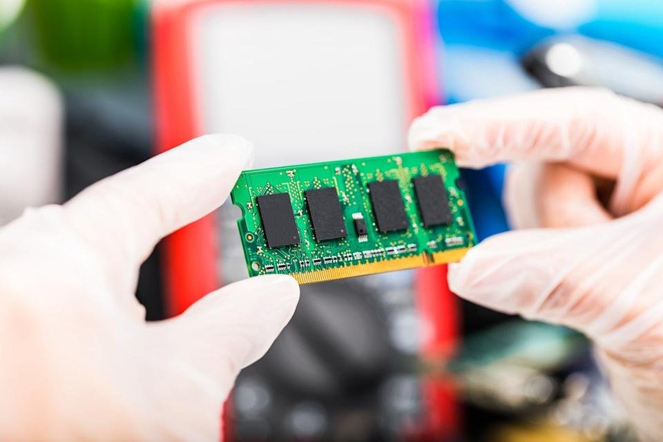 Two gloved hands hold a card with a series of memory chips.