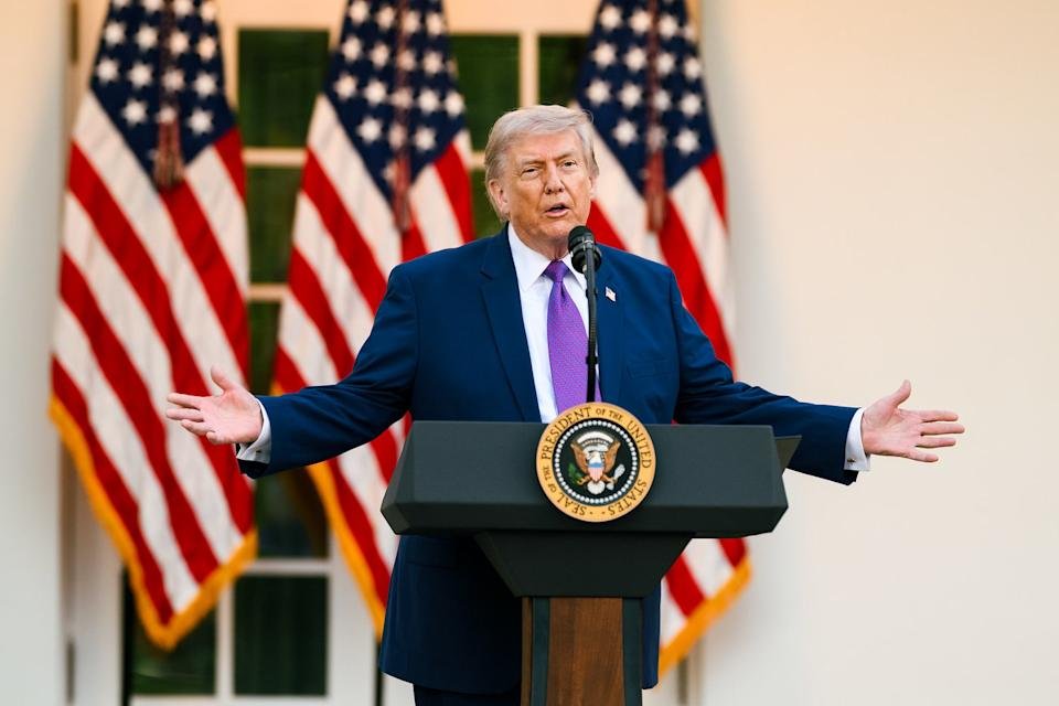 President Trump outside the White House standing at a podium with three American flags behind him.