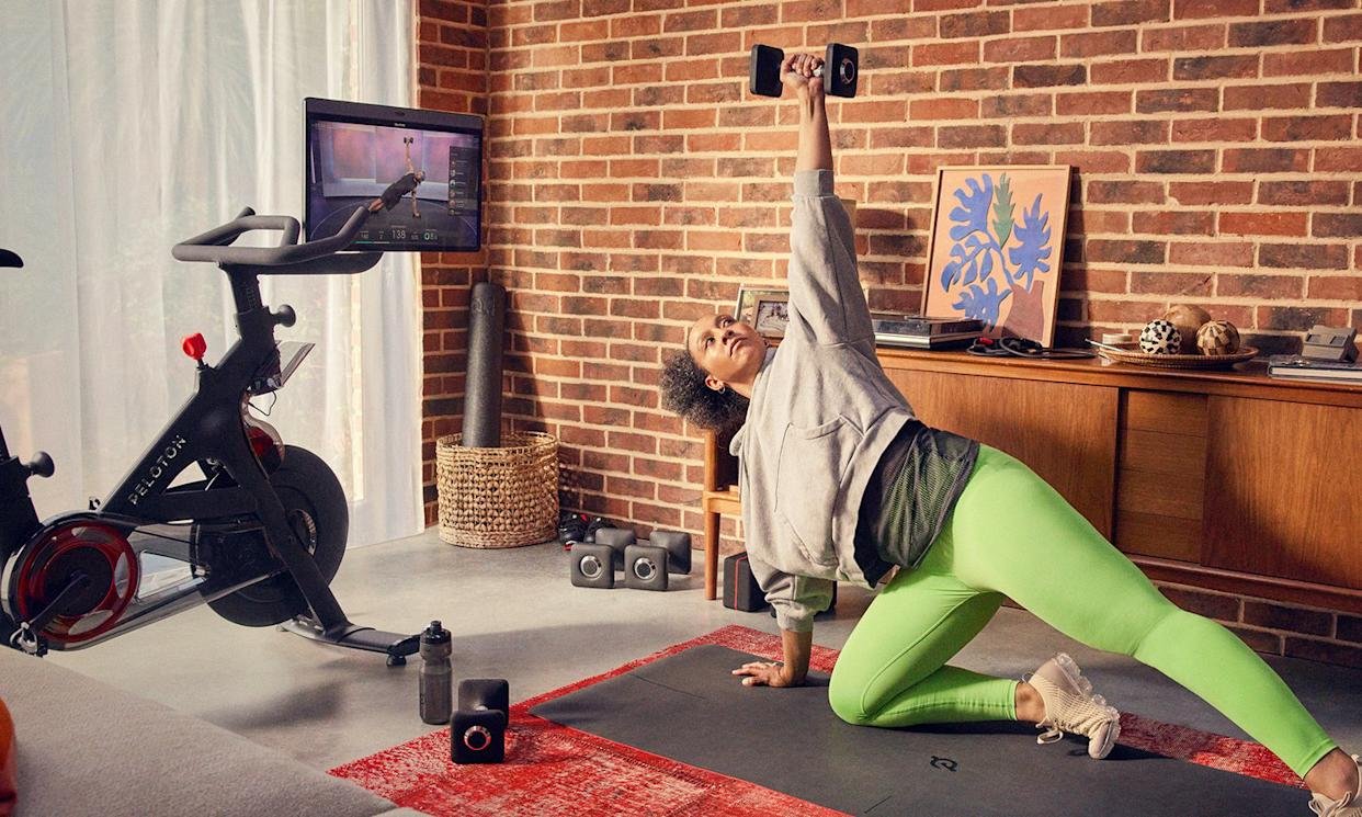 A person working out with free weights while watching a class through the screen on their Peloton Bike.
